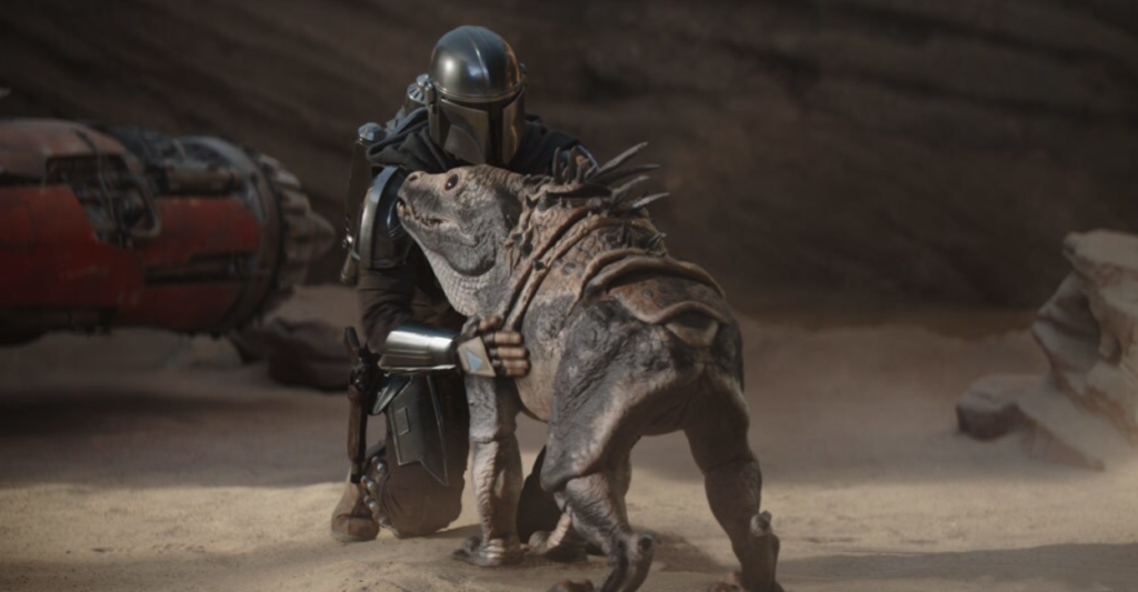 A dog like creature with scaled armor sits in front of a space man